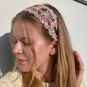 Handvirkat pastellfärgat hårband  - Säljer ett handvirkat diadem i pastellfärger med öppet, blommigt mönster. Färgerna går i rosa, ljusgrönt, lila och blått. Diademet har en bred form och är gjort i mjukt garn, perfekt för en söt och trendig look.
