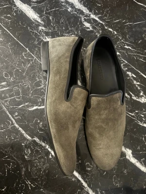Grå/gröna mocka loafers från Limitato - Snygga loafers i grå/grön mocka från Limitato. Skorna har en stilren och minimalistisk design med svarta detaljer runt öppningen och en låg klack. Perfekta för dig som gillar en clean look och vill ha något som sticker ut utan att bli för mycket.