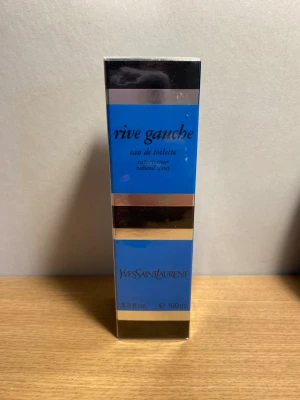 Yves Saint Laurent Rive Gauche EDT 100 ml Oöppnad & Vintage - Yves Saint Laurent Rive Gauche Eau de Toilette 100 ml.  Oöppnad och fortfarande fabriksförseglad.  Vintageparfym som inte längre tillverkas. Har förvarats i familjens ägo under en längre tid. Säljs i befintligt skick, en liten flik har gått upp (se bild 5). Se bilder för skick och detaljer.  Skickas väl emballerad.