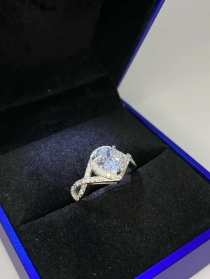 925s silverring med stor klar sten - Snygg 925s silverfärgad ring med en stor, klar rund sten i mitten och mindre gnistrande stenar längs bandet. Ringen har en elegant tvistad design som ger en lyxig känsla.
