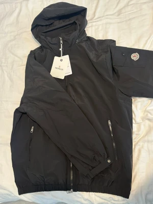 Svart vindjacka från Moncler med huva - Moncler jacka i svart. Ny med tags. Det står 2XL i jackan, men den passar egentligen dig som brukar ha storlek L. Nyskick. Perfekt för dagar då det är vind. Pris kan diskuteras.  