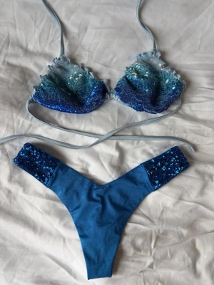Calzedonia bikini - Säljer en fin bikini från Calzedonia med så fina detaljer. Underdelen är enfärgad, fyllt med så fina paljetter längst med sidorna. Överdelen är en triangelmodell med knytband, som är täckt av paljetter i en vacker blå ombré. Den har små volanger längst med sidorna som en extra detalj. Både är köpta separat, tror inte det ordinarie hör ihop, men jag tycker det är väldigt fina tillsammans👩🏽‍❤️‍💋‍👩🏼 Står ingen storlek men skulle säga XS i toppen och Xs/S i trosan. Använd gärna KÖP NU💗