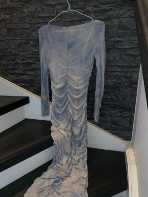 Ljusblå långklänning med rynk - Säljer en elegant ljusblå långklänning med rynkdetaljer längs hela framsidan och baksidan. Första bilden är baksidan, andra är framsidan. Materialet är tunt och stretchigt, perfekt för speciella tillfällen.