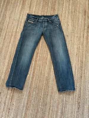 Selvedge Denim - Diesel Industry Bootcut - Ett par klassiska blå jeans med bootcut passform och slitna detaljer vid bensluten. Jeansen har fem fickor, ljusare tvättade partier och kontrastsömmar. Perfekta för en avslappnad och trendig look.