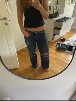 Blå slitna raka low wasted jeans med hål - Säljer ett par blå jeans med raka ben och stora slitningar vid knäna. Jeansen har en avslappnad passform och klassisk femficksdesign. Perfekta för en trendig och avslappnad stil. Materialet är denim i bomull.skriv vid frågor eller pris💕