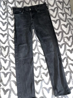 Raka jeans - Säljer ett par svarta jeans med rak passform och klassisk femficksdesign. Jeansen har knapp och dragkedja framtill samt bälteshällor i midjan. Materialet är denim med en lätt tvättad look.
