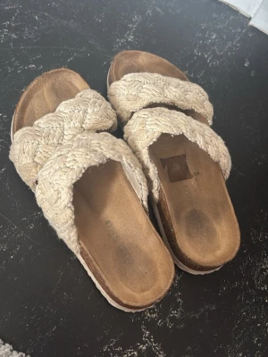 Beige flätade sandaler med platåsula - Säljer ett par beige sandaler med breda, flätade band över foten och platåsula. Ovandelen är i ett grovt tygmaterial som ger en avslappnad vibe. Perfekta för varma dagar och enkla att matcha med olika outfits.