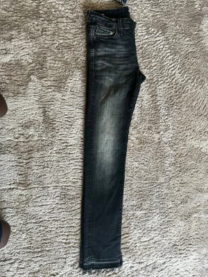 Svarta skinny jeans med rå kant - Säljer ett par svarta skinny jeans med slitna, råa kanter nertill och snygg tvättad effekt längs benen. Jeansen har klassisk femficksmodell och dragkedja. Perfekta för en trendig och avslappnad stil.
