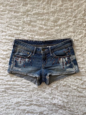 Coola jeansshorts med broderi - Superfina jeansshorts i en snyggt sliten blå tvätt. Shortsen har jättefina, bohemiska broderier i rött, vitt och blått både framtill runt fickorna och på ena bakfickan. De har råa, uppvikta fållar nertill och är i mycket fint skick! Storlek 36 (alla mått finns i bilderna). 💕💕