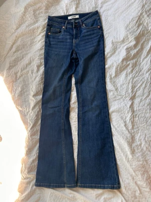 Mörkblå bootcut jeans från kappahl - Säljer ett par mörkblå bootcut jeans från kappahl med klassisk femficksdesign och utsvängda ben. Jeansen har normal midja och är tillverkade i ett mjukt denimtyg. Perfekta för dig som gillar lite skönare jeans.