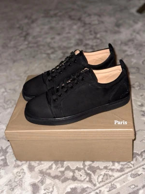 Christian Louboutin skor - Stilrena svarta sneakers med låg profil och klassisk snörning. Skorna har en unik röd sula med grafiskt mönster undertill och beige innersida. Materialet ser ut att vara mocka eller nubuck, vilket ger en lyxig känsla. Perfekta för dig som gillar minimalistisk och exklusiv stil. Använda 1-2 gånger max!