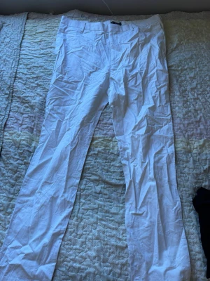 Vita raka chinos - Säljer ett par vita chinos med raka ben och klassisk passform. Byxorna har bälteshällor, fickor fram och bak samt stängs med knapp och dragkedja. Perfekta för en avslappnad och stilren look. 