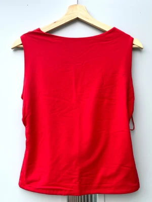 Röd ärmlös topp med drapering - Snygg röd topp med djup draperad urringning i ryggen. Toppen är ärmlös och har en figurnära passform, perfekt för att sticka ut. Tillverkad i mjukt material som känns skönt mot huden.