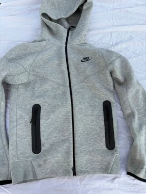 Grå Nike hoodie med dragkedja XS - Grå Nike Tech Fleece zip hoodie  Använd få gånger Ordinarie pris: 1399kr | Säljer för: 800kr  Öppen för andra pris förslag! Hör gärna av dig om du har några frågor