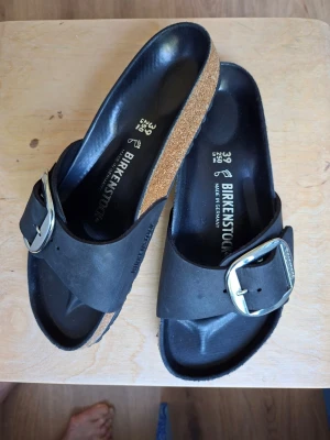 Edgy sandaler, svarta Birkenstock, strlk 39 med spänne i silvermetall - Modell Madrid Big Buckle. Fotbädden är formad för extra komfort med passform normal. Längd: 246-250 mm och bredd: 94-102 mm. Täcksula i svart läder. Lätt, snygg sandal. Nyinköpt, men saknar kvitto. Har använts i 20 minuter. Det finns inga defekter, missfärgningar eller förslitningar.