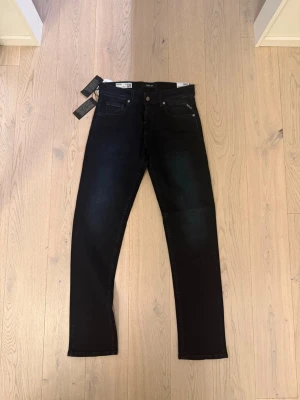 Svartblåa jeans från Replay modell grover 29W L 32 - Snygga svartblåa jeans från Replay, modell Grover med klassisk femficksdesign och diskreta sömmar. Jeansen har en modern passform och är tillverkade i stretchigt denimtyg för extra komfort. Perfekta för dig som gillar en stilren look. W29 L 32