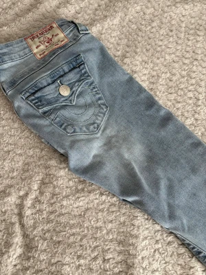 True Religion ljusblå flare jeans - Säljer ett par ljusblå True Religion Joey Low Rise Flare jeans med snygga kontrastsömmar och ikonisk fickdetalj bak. Jeansen har låg midja och utsvängda ben, perfekta för en avslappnad men trendig look. Pris kan diskuteras vid snabbt köp