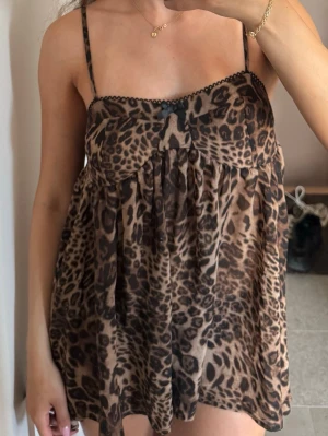 Leopardmönstrad kort klänning - Säljer en kort klänning med leopardmönster och tunna axelband. Klänningen har en lös passform och är tillverkad i ett lätt, flödande material. Detaljer som liten rosett framtill och spetskant vid bysten ger en söt touch.