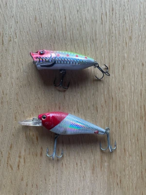 Två fiskedrag i rött och silver - Säljer två fiskedrag med krokar, ena med röd och silverfärgad kropp och holografiska detaljer, den andra med röd nos och silverglänsande kropp samt plastsked framtill. Perfekta för fiske efter rovfisk. Båda har realistiska ögon och flera trekrokar. Draget högst upp är ett ytbete 