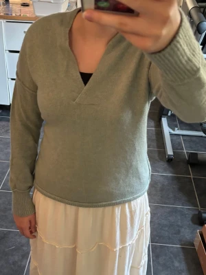 Grå v-ringad stickad tröja YAYA - Mysig grå stickad tröja från YAYA med djup v-ringning och avslappnad passform. Tröjan har långa ärmar, breda ribbade muddar och något längre bakstycke. Perfekt för lager på lager och enkel att styla till jeans eller kjol. I storlek XS.
