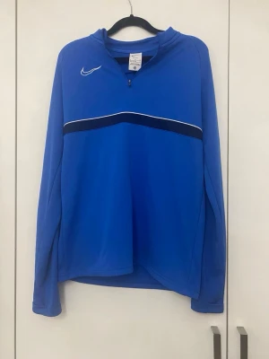 Nike träningströja i blått - Nike träningströja i blått med mörkblå och vit rand över bröstet Storlek 158-170cm Mycket fint skick