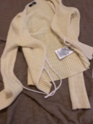 Ljusgul ribbad omlottkofta - Trendig ljusgul ribbad omlottkofta med långa ärmar och knytband i midjan. Koftan har en mjuk och stretchig känsla, perfekt att slänga över en topp. Snygg detalj med vita kanter längs öppningen. Passar till många olika stilar.