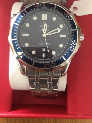 Omega Seamaster 300m - Snygg Omega Seamaster klocka med blå urtavla och vågmönster. Boetten och länken är i blankt rostfritt stål. Klockan har datumvisning vid 6 och tydliga indexmarkeringar. Roterande blå bezel och klassisk sportig design. Perfekt accessoar för dig som gillar stilrena detaljer.