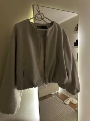 Beige bomberjacka från Zara - Säljer en beige bomberjacka från Zara med dragkedja framtill och två fickor. Jackan har en croppad passform och långa ärmar. Använd 1 gång.