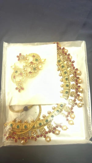 Guldigt halsband med pärlor och stenar - Säljer ett elegant halsband i guldfärgad metall med gröna och röda stenar samt stora pärlor. Halsbandet har en detaljrik design med blommönster och matchande örhängen. Perfekt för dig som gillar färgstarka accessoarer och unik stil.