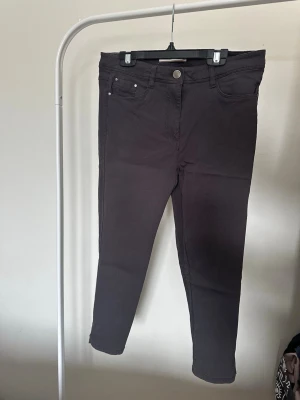 Mörkgrå caprijeans - Säljer ett par mörkgrå capri jeans med klassisk femficksdesign och raka ben. Jeansen har knappstängning och är tillverkade i ett mjukt material som ger en skön passform. Perfekta för dig som gillar en enkel och stilren look.
