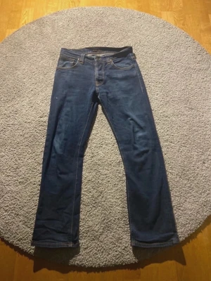 Nudie jeans mörkblå raka - Snygga mörkblå jeans med raka ben och klassisk femficksdesign. Jeansen har kontrastsömmar och är tillverkade i ett slitstarkt denimtyg. Passar perfekt till en avslappnad stil och är ett måste i garderoben.   