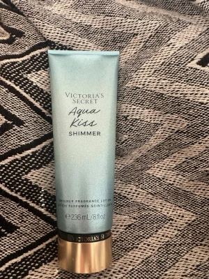 Victoria's Secret Aqua Kiss Shimmer lotion 236 ml  - Victoria's Secret Aqua Kiss Shimmer är en skimrande kroppslotion i en ljusblå tub med guldigt lock. Innehåller 236 ml, är knappt använd har en skimrande effekt på huden. Likar så fräscht och gott. 