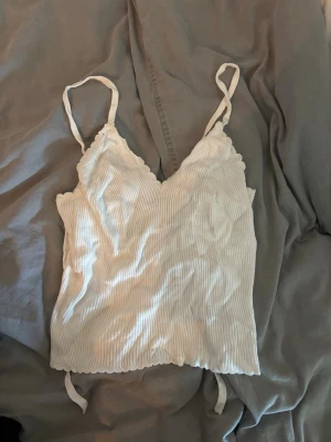 Vit ribbad linnetopp med snörning - Säljer en söt vit ribbad linnetopp med tunna axelband och v-ringad hals. Toppen har knytning i ryggen och superfin till sommaren! 💗