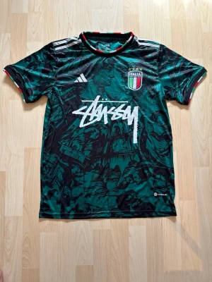 Italien x Stüssy Teal Green Special Edition Kit - Stilren fotbollströja i helt nytt skick. Tröjan är inte använd en endaste sekund. Italien tröjan är kombinerad med det exklusiva streetwear märket Stüssy.