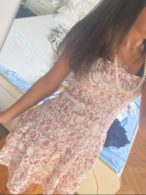 Vit och röd blommig kortklänning - Söt kortklänning med vitt och rött blommigt mönster. Klänningen har en lätt utsvängd form och är ärmlös, perfekt för varma dagar. Materialet känns mjukt och luftigt, troligen bomull. Passar dig som gillar romantiska och somriga vibes.