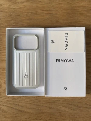 Rimowa iPhone 17 Pro Max silver mobilskal aluminium - Snyggt mobilskal från Rimowa i silverfärgad aluminium med ikoniska räfflade linjer. Skalets design är stilren och modern, med en robust känsla och logotyp på framsidan. Perfekt för dig som vill ha ett exklusivt och tåligt skydd till din mobil.