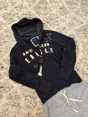 Mörkblå hoodie från American Eagle - Säljer en mörkblå hoodie från American Eagle Outfitters med tryck på bröstet och broderade detaljer | Size S och passar true to size | Pris och andra funderingar kan diskuteras