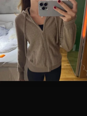 Beige zip-hoodie med fickor - Mysig beige hoodie med dragkedja och två framfickor. Tröjan har huva med snören och ribbade muddar vid ärmslut och nederkant. Perfekt för en avslappnad look och passar till jeans eller leggings.