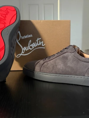 Gråa Christian Louboutin  - Snygga gråa sneakers från Christian Louboutin i mjuk mocka med klassisk röd sula. Helt nya ej rörda! Hör av dig privat vid intresse, kan gå ner i pris!