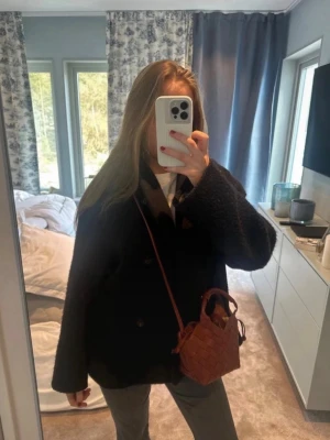 Arket kappa - Säljer en svart, dubbelknäppt kappa med bred krage från Arket. Kappan är tillverkad i ett ulligt material som ger en mysig och stilren look. Perfekt för kyliga dagar och passar till många outfits. Den har tyvärr spruckit lite i innerfodret men det syns inte när man har på sig den och fickan fungerar fortfarande.