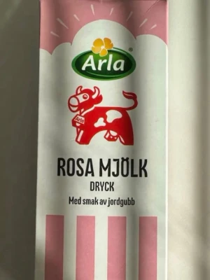 Arla Rosa Mjölk med jordgubbssmak - Säljer en förpackning Rosa Mjölk från Arla, en dryck med smak av jordgubb. Kartongen har rosa och vita ränder samt en röd ko på framsidan. Perfekt för dig som gillar mjölk med fruktig twist.
