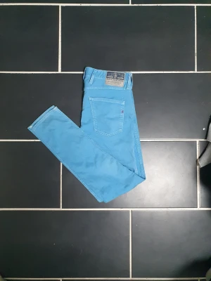 Replay anbass - Snygga ljusblå jeans från Replay med klassisk femficksdesign och röd logodetalj på bakfickan. Jeansen har raka ben och är tillverkade i mjukt denimtyg som ger en skön känsla. Perfekta för dig som vill sticka ut med färg.