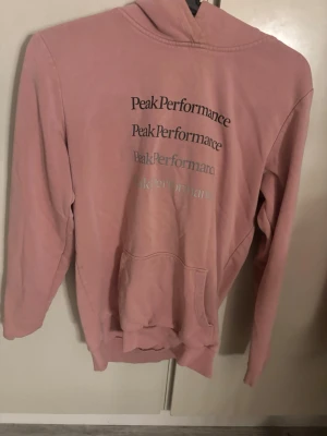 Rosa hoodie från Peak Performance - Rosa hoodie från Peak Performance med tryckt logga i flera olika nyanser på bröstet. Hoodien har en stor huva och en klassisk magficka framtill. Materialet är mjukt och bekvämt, perfekt för chill dagar. Snygg och enkel design som passar till jeans eller joggers. Pris kan diskuteras!