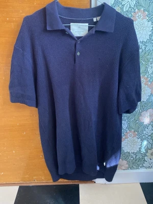 Mörkblå stickad topp från Jack & Jones - Säljer en mörkblå stickad topp från Jack & Jones med klassisk krage och knappar framtill. Toppen är gjord i bomull och har korta ärmar. Perfekt för dig som gillar en stilren och bekväm look med lite struktur.