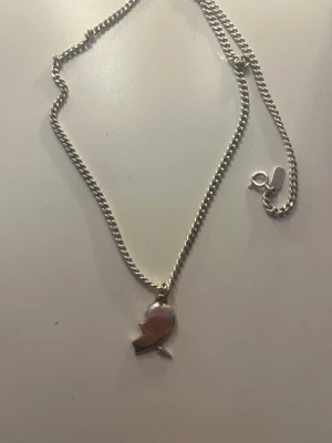 Silverhalsband från Maria Nilsdotter  - Snyggt halsband i silverfärg med en kedja och en berlock. Kedjan har en klassisk karbinhake och en liten bricka vid låset. Perfekt accessoar för dig som gillar stilrena detaljer.