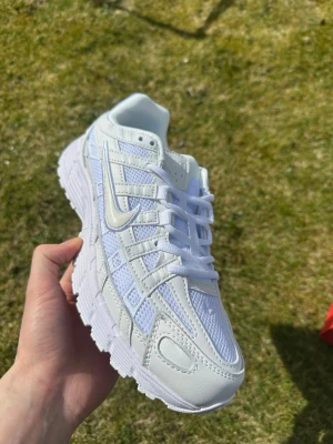 Vita Nike P-6000 sneakers - Säljer ett par fräscha vita Nike P-6000 sneakers med mesh och syntetiska överdrag. Skorna har en chunky sula, klassisk Nike Swoosh på sidan och vita skosnören. Perfekta för dig som gillar sportig och clean stil.