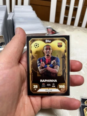 Match Attax FC Barcelona samlarkort - Säljer ett Match Attax samlarkort från Topps med FC Barcelona-tema. Kortet har guldfärgad ram och motiv av en spelare Raphinha i blå-röd tröja. Perfekt för dig som gillar fotboll och samlar på trading cards.