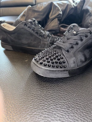 Christian louboutin - Snygga svarta sneakers från Christian Louboutin i mocka med svarta nitar på tån. Klassisk låg modell med svarta skosnören och diskret logga på hälen. Perfekta för dig som vill sticka ut med en edgy och exklusiv stil.