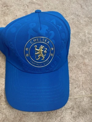 Blå Chelsea FC keps - Snygg blå keps med Chelsea FC:s ikoniska lejonlogga i guld framtill och broderad text bak. Justerbar rem för perfekt passform. Tillverkad i slitstark bomull, perfekt för dig som vill visa vilket lag du hejar på.