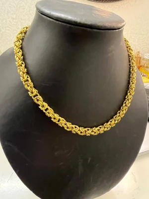 Guldpläterat kedjehalsband - Snyggt halsband i guldpläterad metall med en chunky, flätad kedjedesign. Halsbandet har en unik struktur med tätt sammanlänkade länkar som ger ett exklusivt och trendigt intryck. Perfekt för dig som vill sticka ut med accessoarerna.